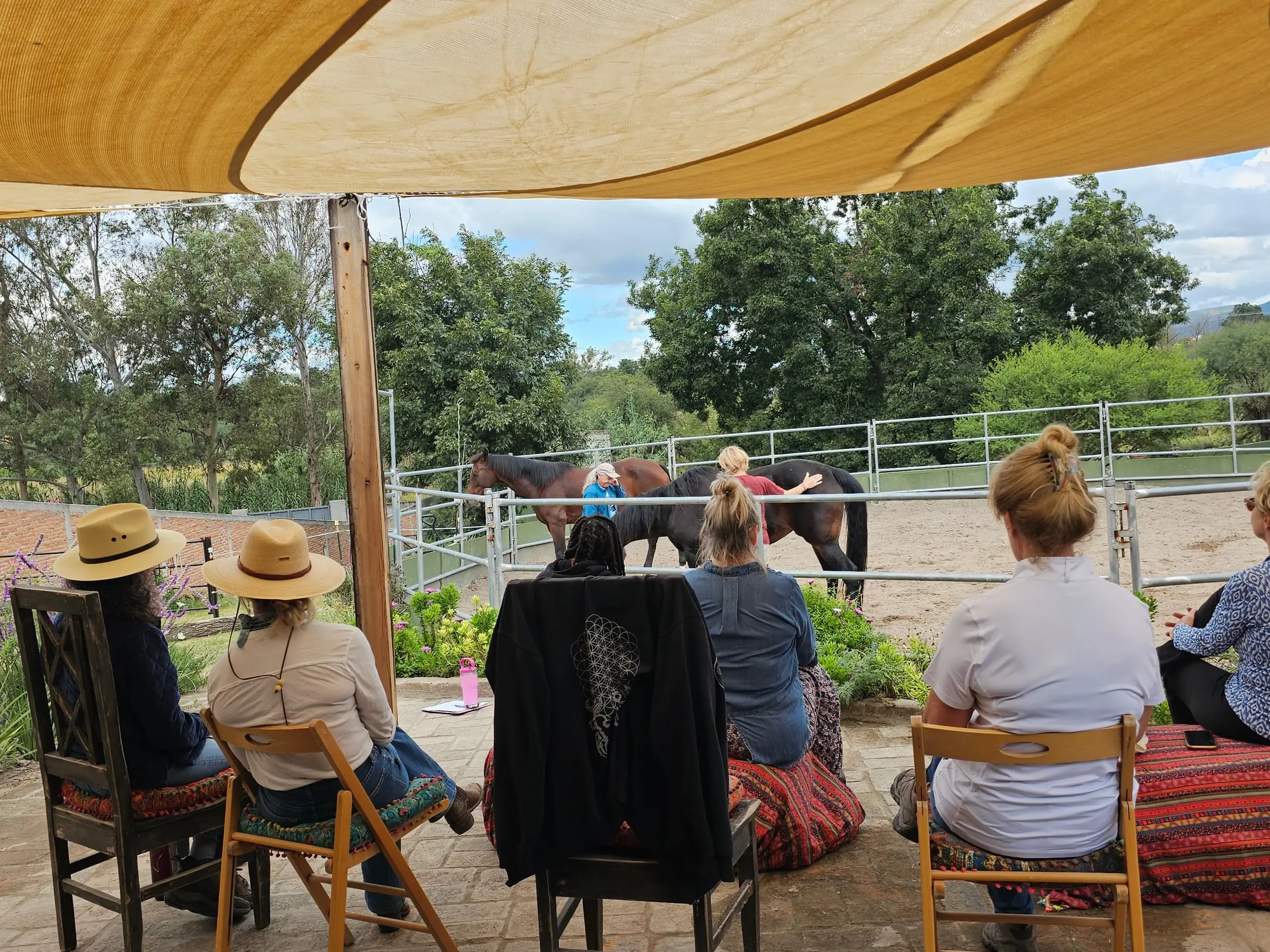 Women watching from the shade as one of the circle works with a horse in the round pen at Rancho Baile de la Luna