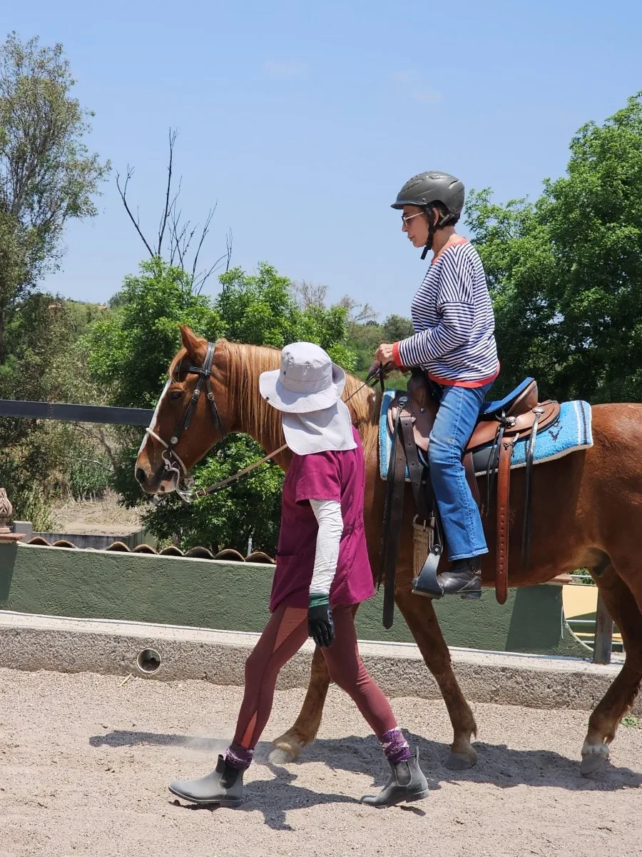 Un niño montando en el ruedo de Rancho Baile de la Luna mientras un adulto lleva al caballo